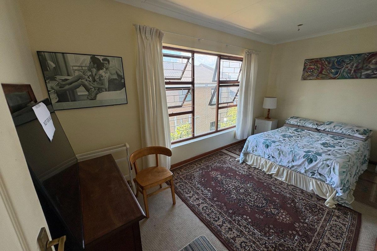 A bedroom featuring a large window with security bars, neutral wall finishes, and carpeted flooring.