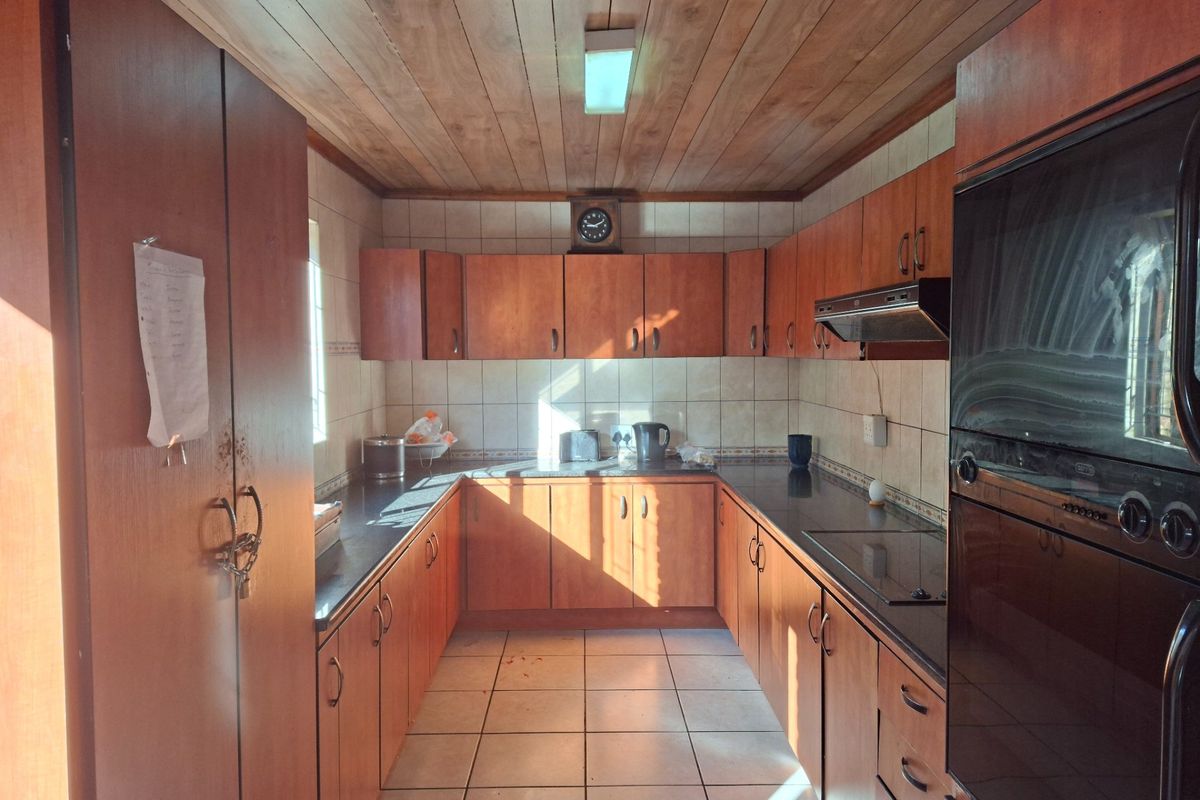 A functional U-shaped kitchen featuring wood-paneled ceilings, tiled flooring, built-in cabinetry, and integrated oven and hob.