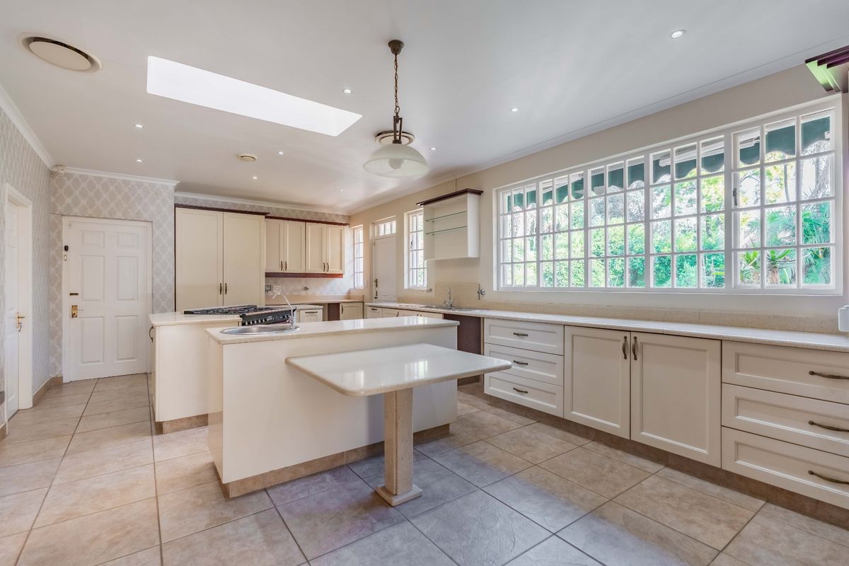 Spacious kitchen featuring ample built-in cabinetry, stone countertops, a central island with a gas hob, and a large skylight providing natural light.