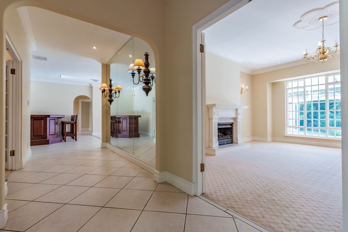 Spacious living area featuring a classic fireplace with mantelpiece, tiled and carpeted flooring, and a mirrored wall leading to a built-in bar area.