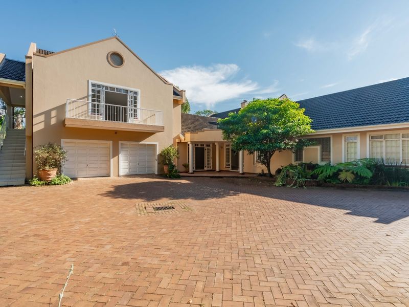 Spacious front exterior view of a townhouse featuring a large brick-paved driveway, double garage, and an upper-level balcony with an external staircase.