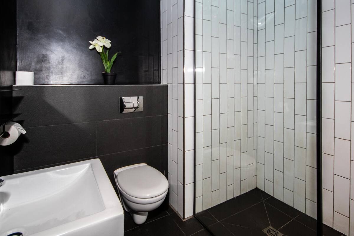Modern bathroom featuring a walk-in shower with white subway tiles, black floor tiles, and a wall-mounted toilet.