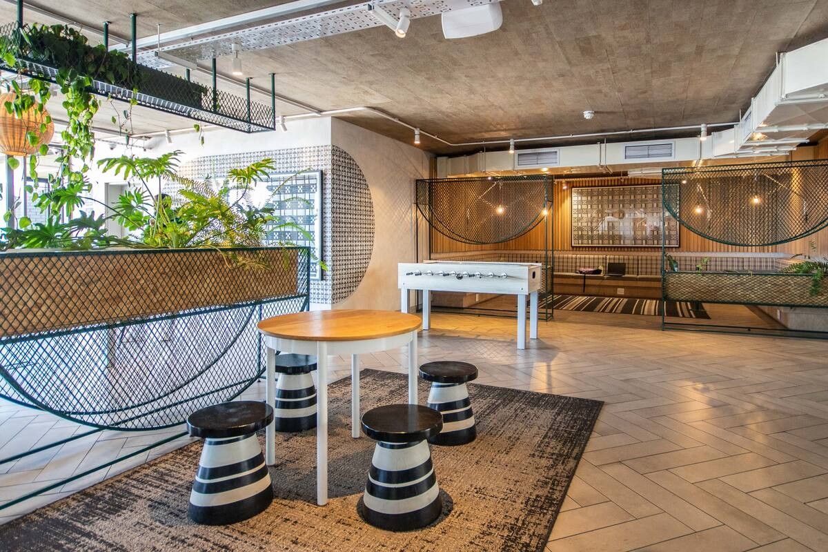 A modern, industrial-style communal living area featuring exposed concrete ceilings, herringbone tiled flooring, and integrated decorative metal mesh partitions.