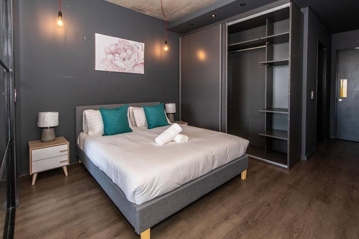 Modern bedroom featuring dark grey walls, exposed concrete ceiling, wood-look flooring, and a large built-in wardrobe with open shelving.