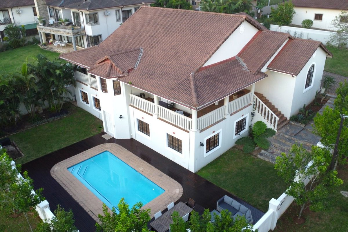 Aerial view of a two-story residential property featuring a tiled roof, wrap-around balcony, swimming pool, and landscaped garden area.