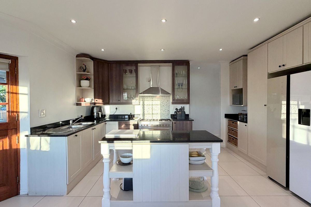 Modern kitchen featuring a central island, granite countertops, stainless steel extractor fan, and ample cabinetry with integrated storage solutions.