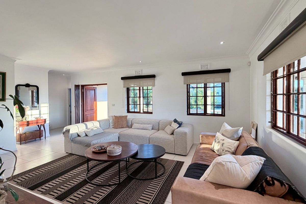 A bright and spacious living room featuring tiled flooring, recessed downlighting, and large timber-framed windows that provide ample natural light.