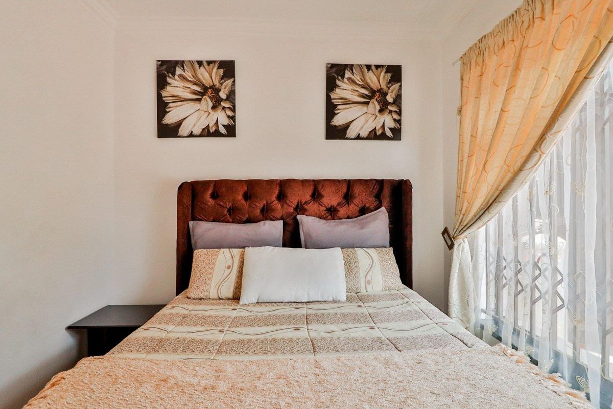 A well-lit bedroom featuring neutral walls, a window with curtain treatments, and a central sleeping area.