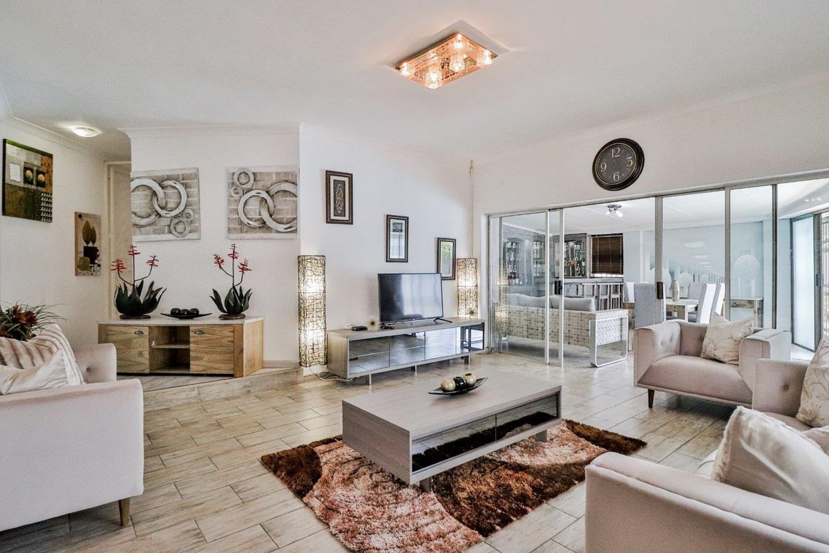 Spacious living room featuring tiled flooring, a decorative ceiling light fixture, and large sliding glass doors leading to an adjacent sunroom or patio area.