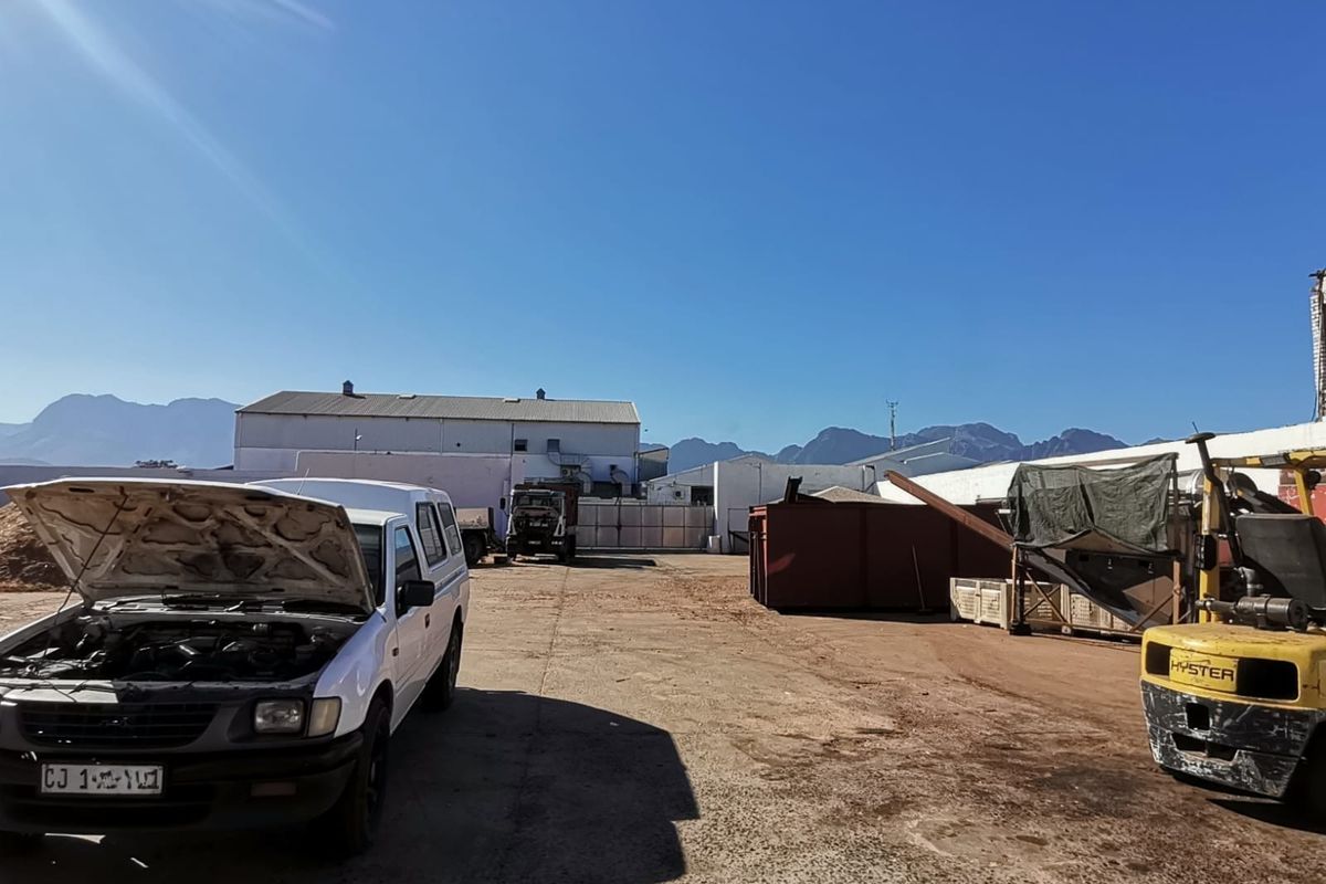 Exterior view of an industrial yard featuring a large concrete workspace, surrounding warehouse structures, and mountain views in the background.