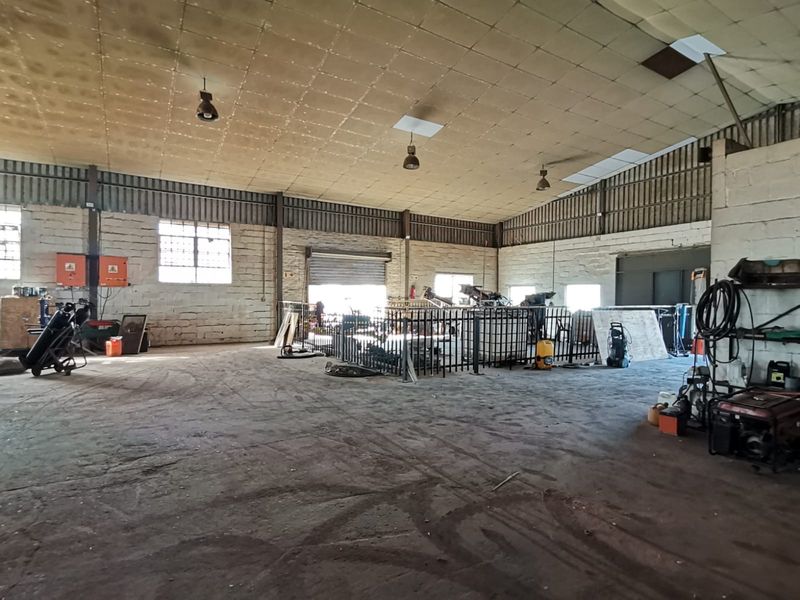 Spacious industrial warehouse featuring high ceilings, exposed brick walls, concrete flooring, and large roller shutter access, suitable for various commercial or manufacturing operations.