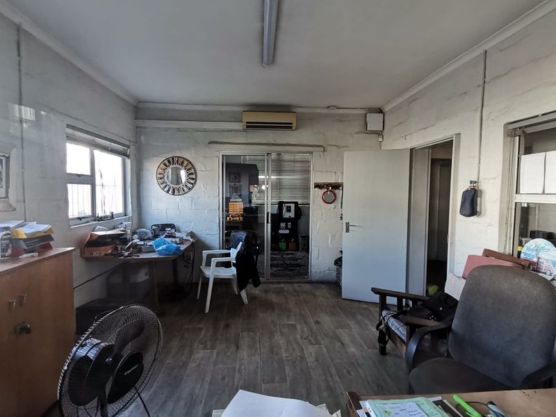 An industrial office space featuring exposed brick walls, wood-look flooring, a wall-mounted air conditioning unit, and sliding glass door access to an adjacent room.