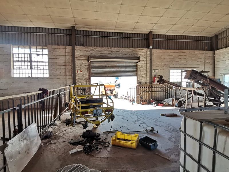 Industrial warehouse space featuring high ceilings, roller shutter door access, and exposed brick walls, suitable for workshop or storage use.