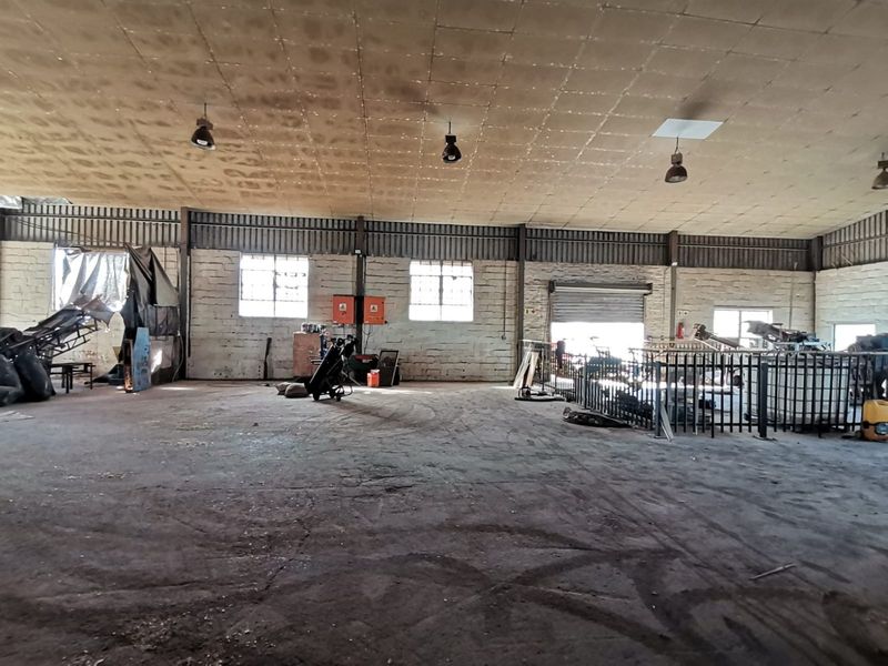 Spacious industrial warehouse featuring high ceilings, exposed brick walls, large roller shutter door access, and functional overhead lighting.