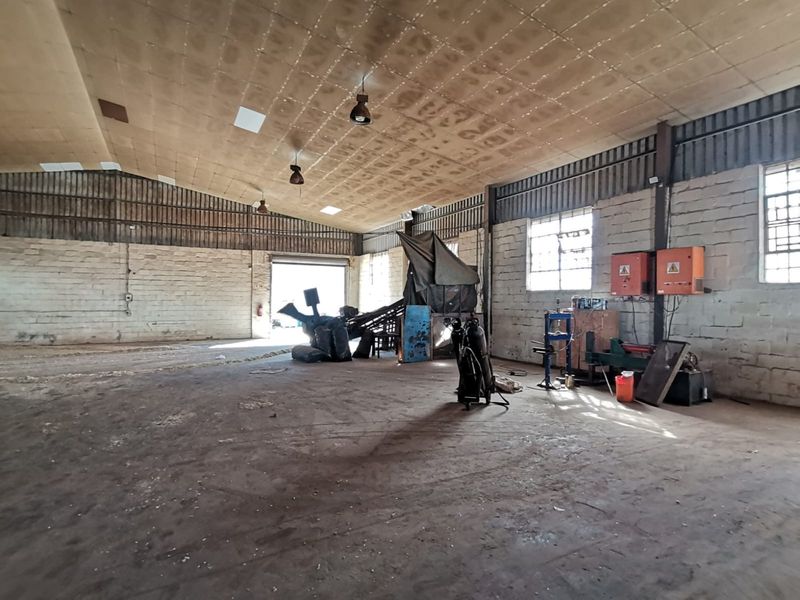 Spacious industrial warehouse featuring high ceilings, exposed brick walls, concrete flooring, and large roller shutter door access.