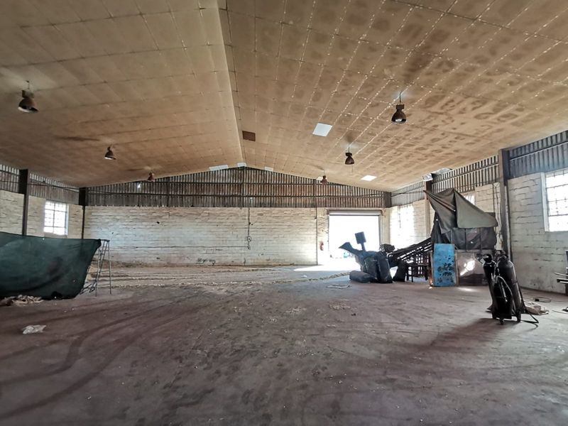 Spacious industrial warehouse featuring high ceilings, exposed brick walls, concrete flooring, and large access points suitable for storage or manufacturing operations.