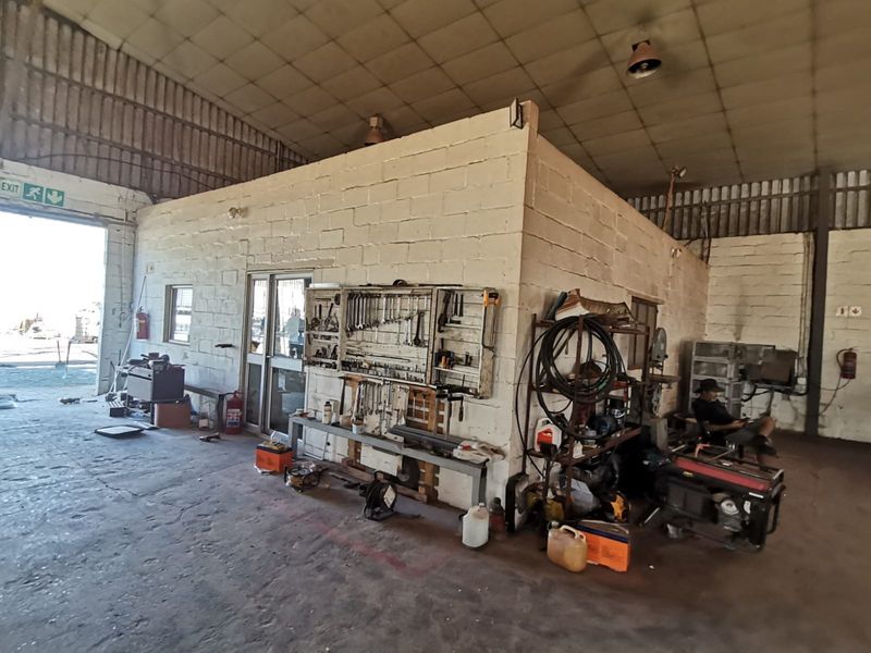 Industrial workshop space featuring high ceilings, exposed masonry walls, and a dedicated partitioned office area with direct access to the exterior yard.