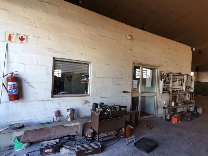 Industrial workspace featuring exposed block walls, concrete flooring, a built-in tool storage rack, and a glass-paneled office partition door.