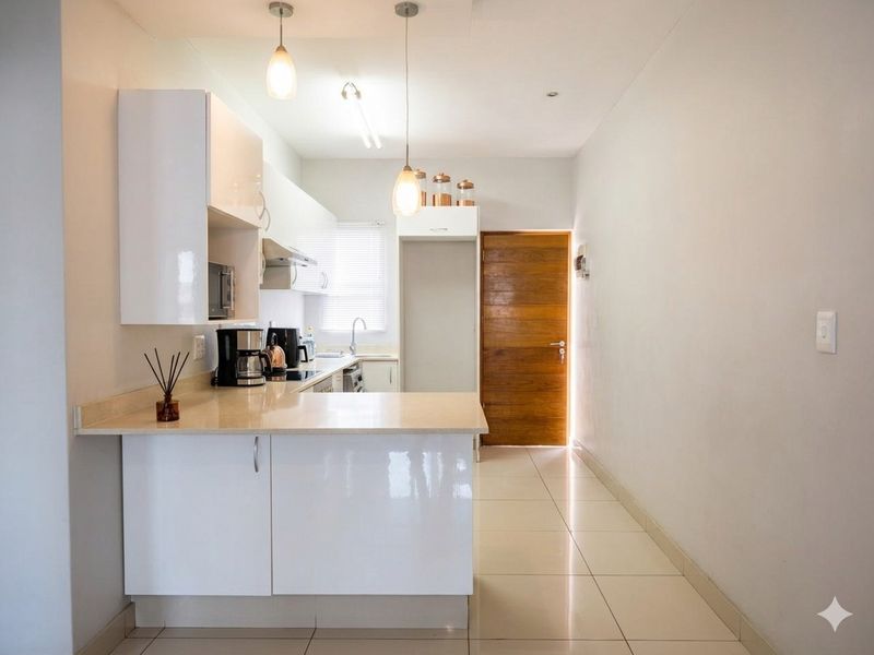 Modern kitchen featuring white high-gloss cabinetry, stone countertops, integrated appliances, and tiled flooring, leading to a wooden door.