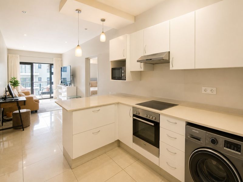 Modern open-plan kitchen featuring sleek white cabinetry, stone countertops, integrated oven, hob, extractor fan, and built-in microwave, flowing into a bright living area.
