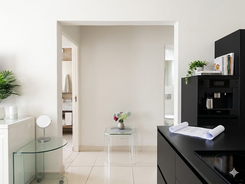 A modern interior view featuring a sleek black kitchen unit and tiled flooring, with doorways leading to adjacent bathroom spaces.