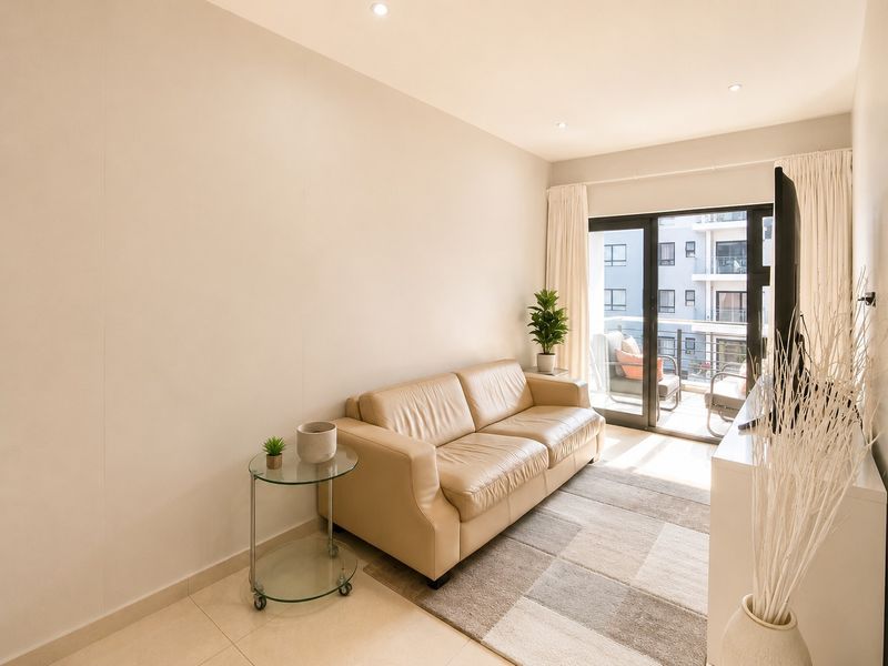 A bright living room featuring tiled flooring, recessed ceiling lighting, and sliding glass doors that open onto a private balcony.