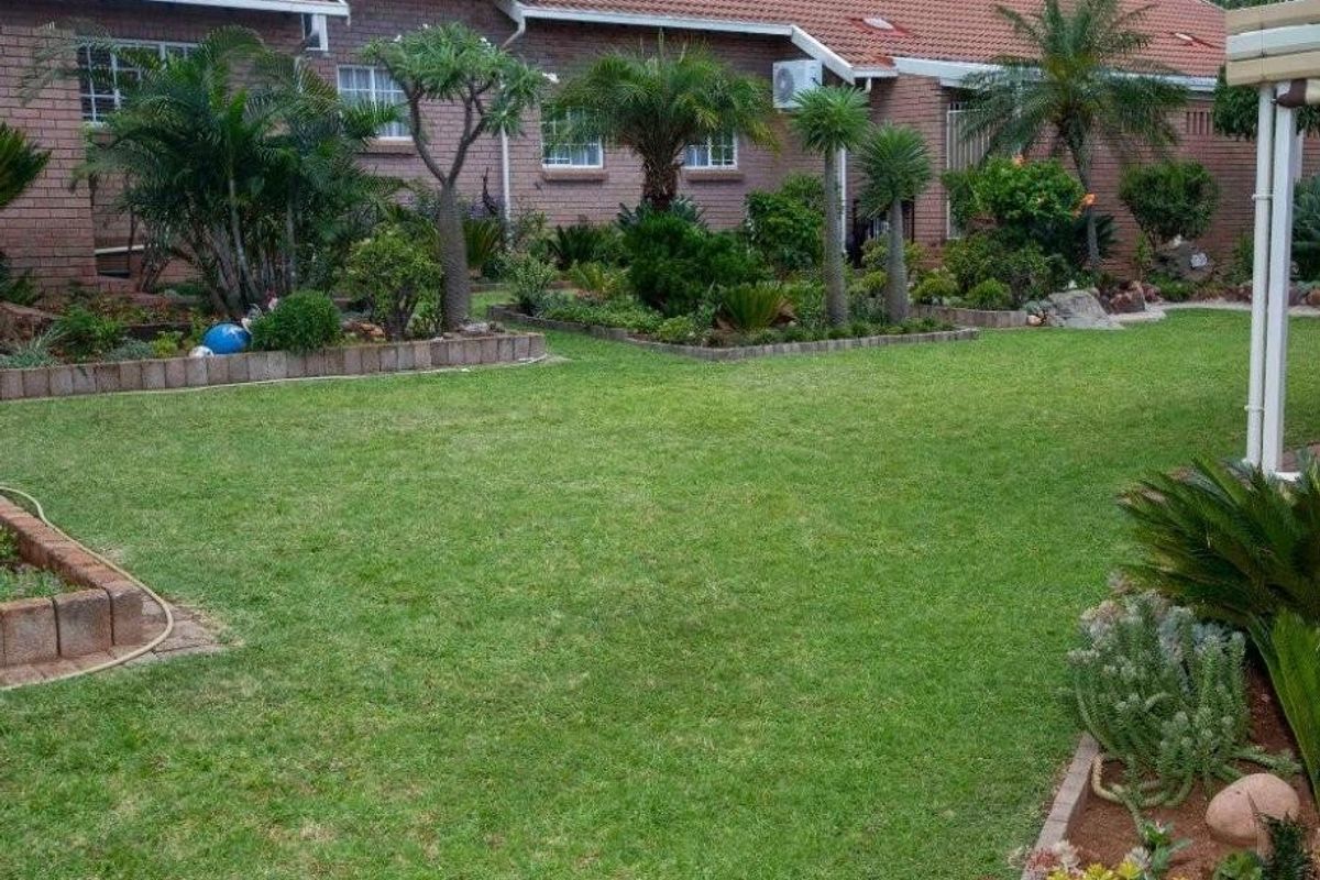 A well-maintained rear garden featuring a manicured lawn, established landscaping, and brick-edged garden beds set against the townhouse exterior.