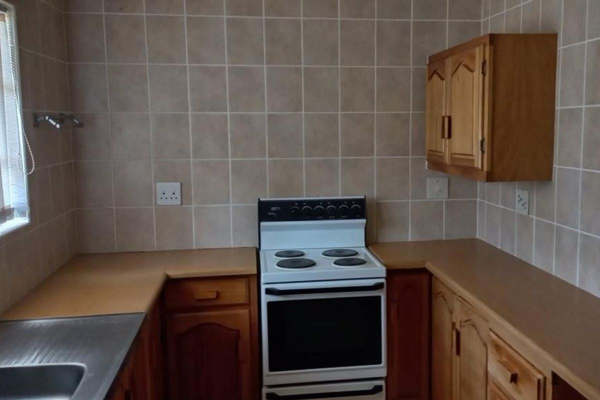 A functional kitchen featuring wooden cabinetry, tiled walls, and a freestanding electric stove with oven.