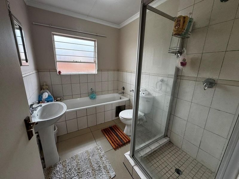 A functional bathroom featuring a pedestal basin, a built-in bathtub, and a separate glass-enclosed shower with tiled walls and flooring.