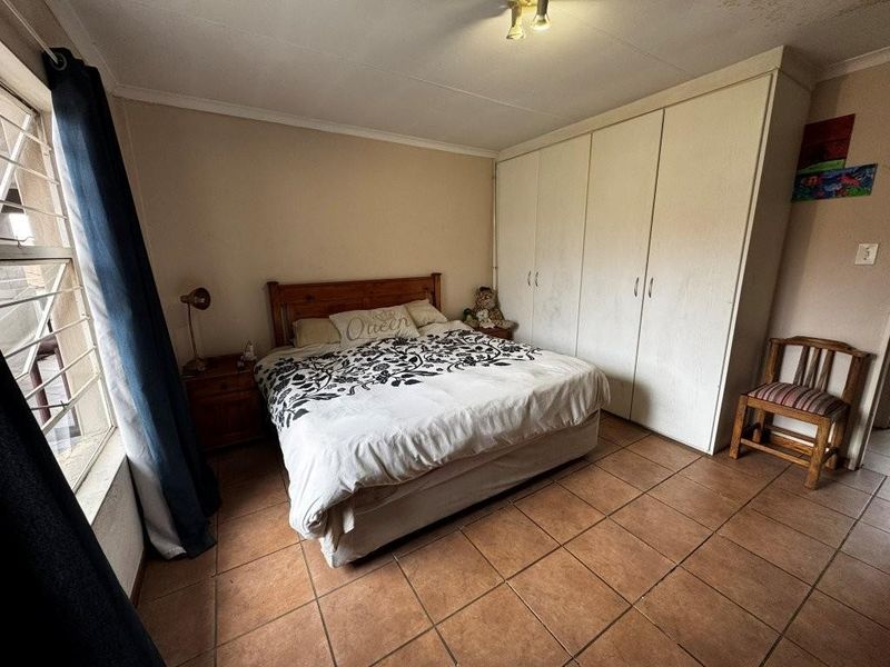 A bedroom featuring built-in cupboards, tiled flooring, and a window with security bars.