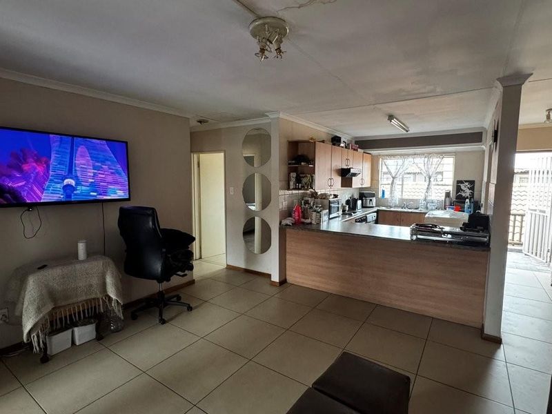 Open-plan living and kitchen area featuring tiled flooring, wooden cabinetry, and a breakfast counter, providing a functional layout for daily living.