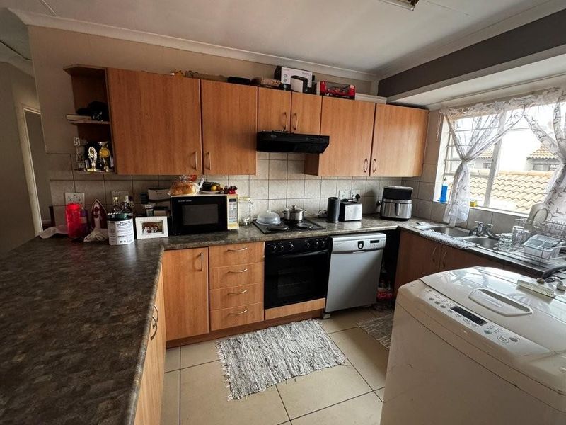 Functional kitchen featuring wood-look cabinetry, laminate countertops, built-in oven, extractor fan, and a double-basin sink with tiled flooring.