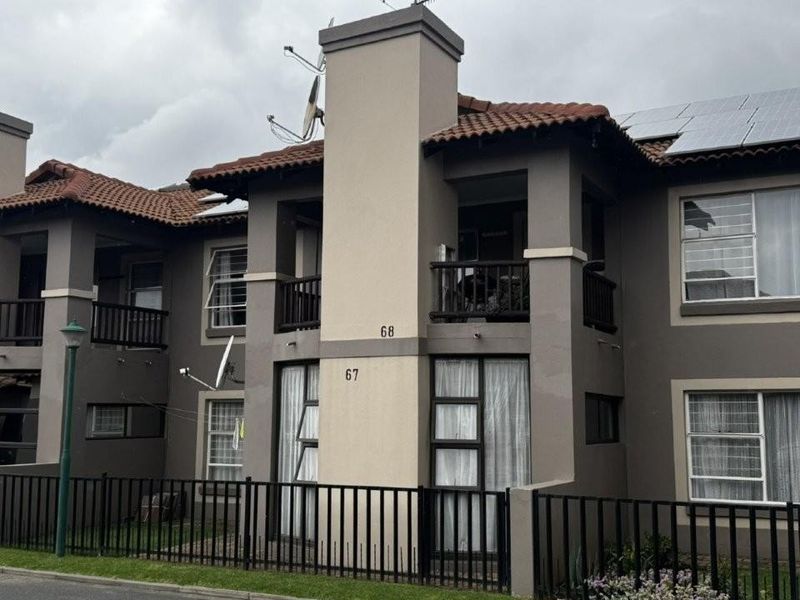 Exterior view of a multi-story apartment complex featuring tiled roofing, private balconies, and ground-floor access with perimeter fencing.