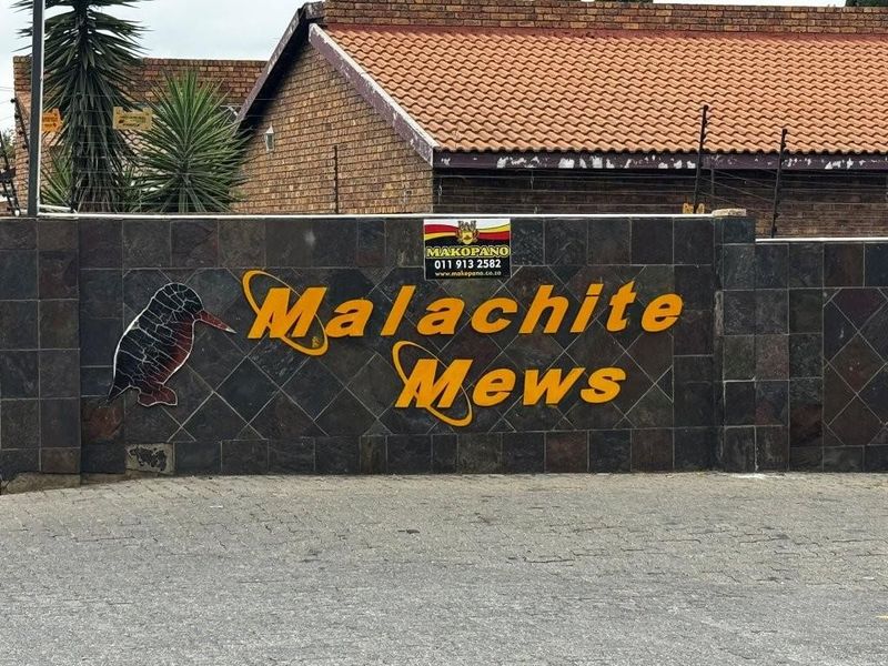 Entrance signage for Malachite Mews apartment complex featuring stone-clad wall and security fencing.