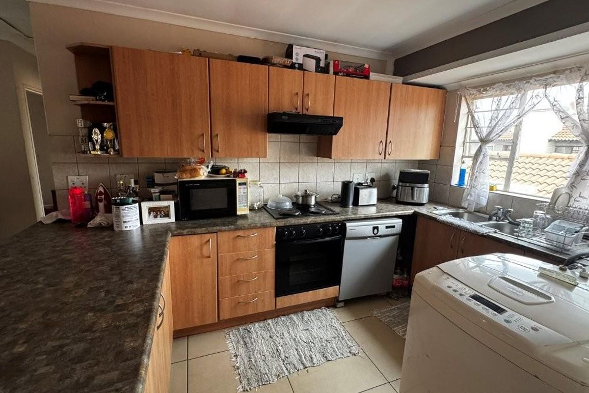 Functional kitchen featuring wood-look cabinetry, laminate countertops, built-in oven, extractor fan, and a double-basin sink with tiled flooring.
