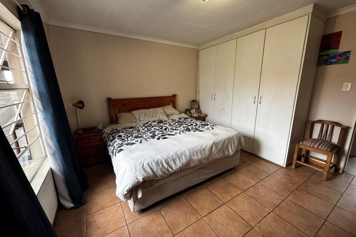 A bedroom featuring built-in cupboards, tiled flooring, and a window with security bars.