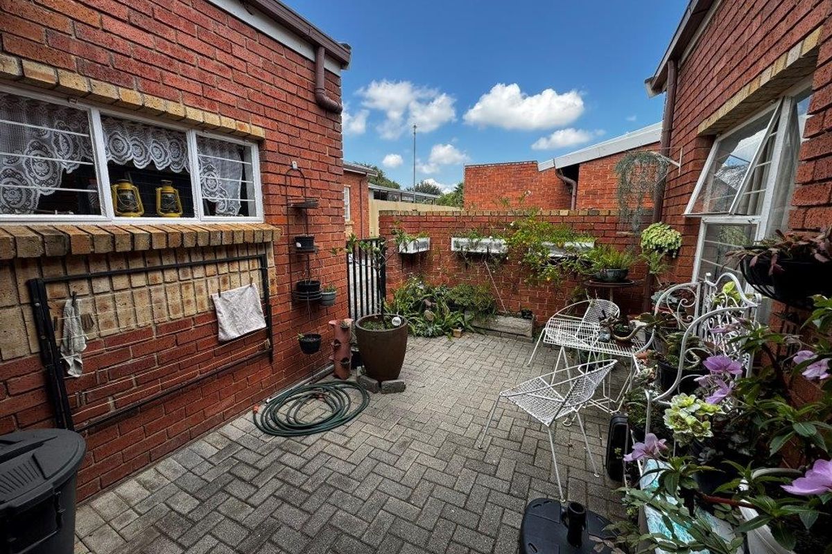 A private paved courtyard area enclosed by face-brick walls, featuring security bars on windows and a secure gated access point.