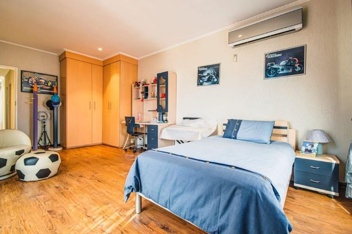 A spacious bedroom featuring built-in wooden cabinetry, laminate flooring, and a wall-mounted air conditioning unit.