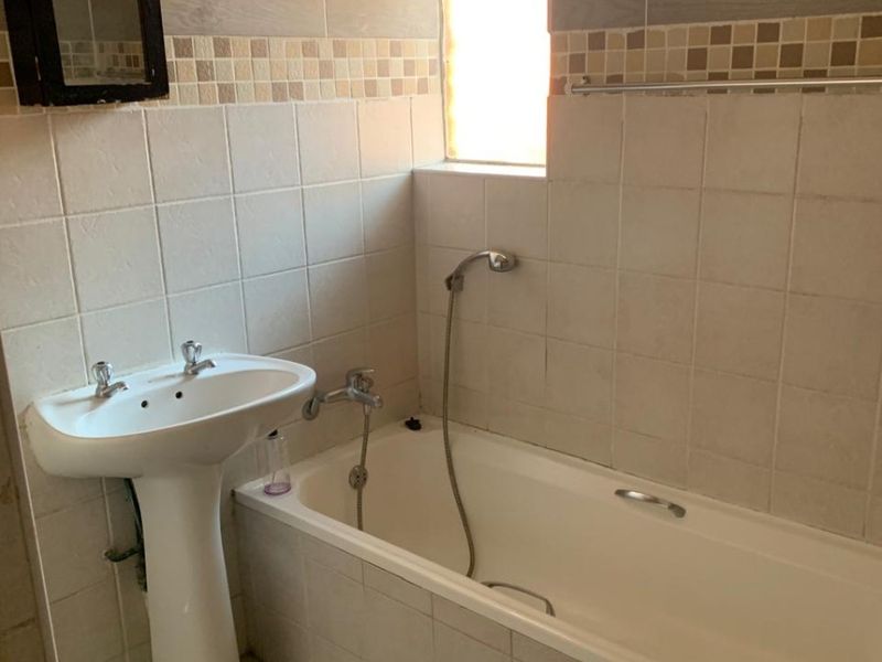 A functional bathroom featuring a pedestal basin, bathtub with handheld shower mixer, and neutral wall and floor tiling.