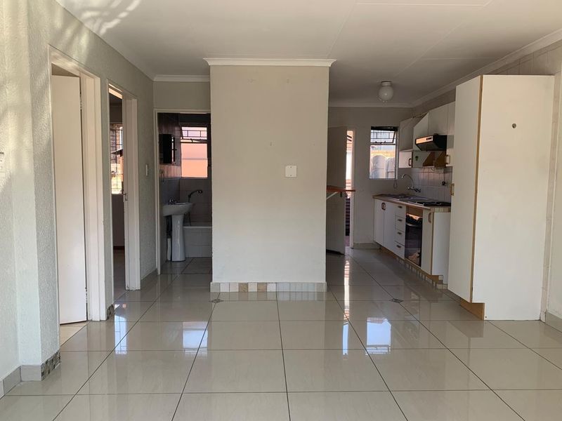 Open-plan living area featuring tiled flooring, a functional kitchen with built-in appliances, and direct access to an adjacent bathroom.