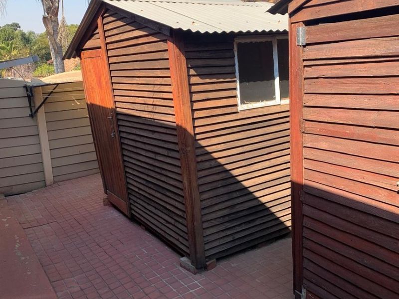 Exterior view of timber utility sheds situated on a brick-paved area, showing signs of weathering and age.
