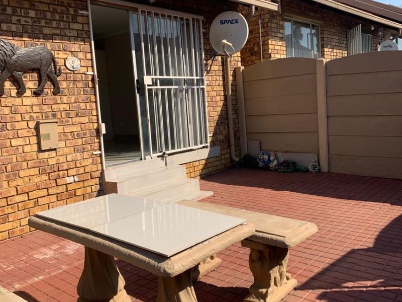 A rear exterior view of the townhouse featuring a paved patio area, brick facade, and secure sliding door access.