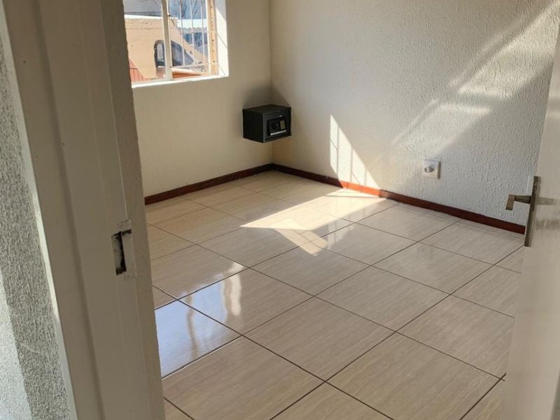 A bright, empty bedroom featuring neutral tiled flooring, a built-in wall safe, and security bars on the window.