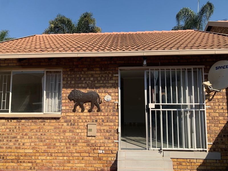 Rear exterior view of a face brick townhouse featuring a tiled roof, security gate, and sliding door access.