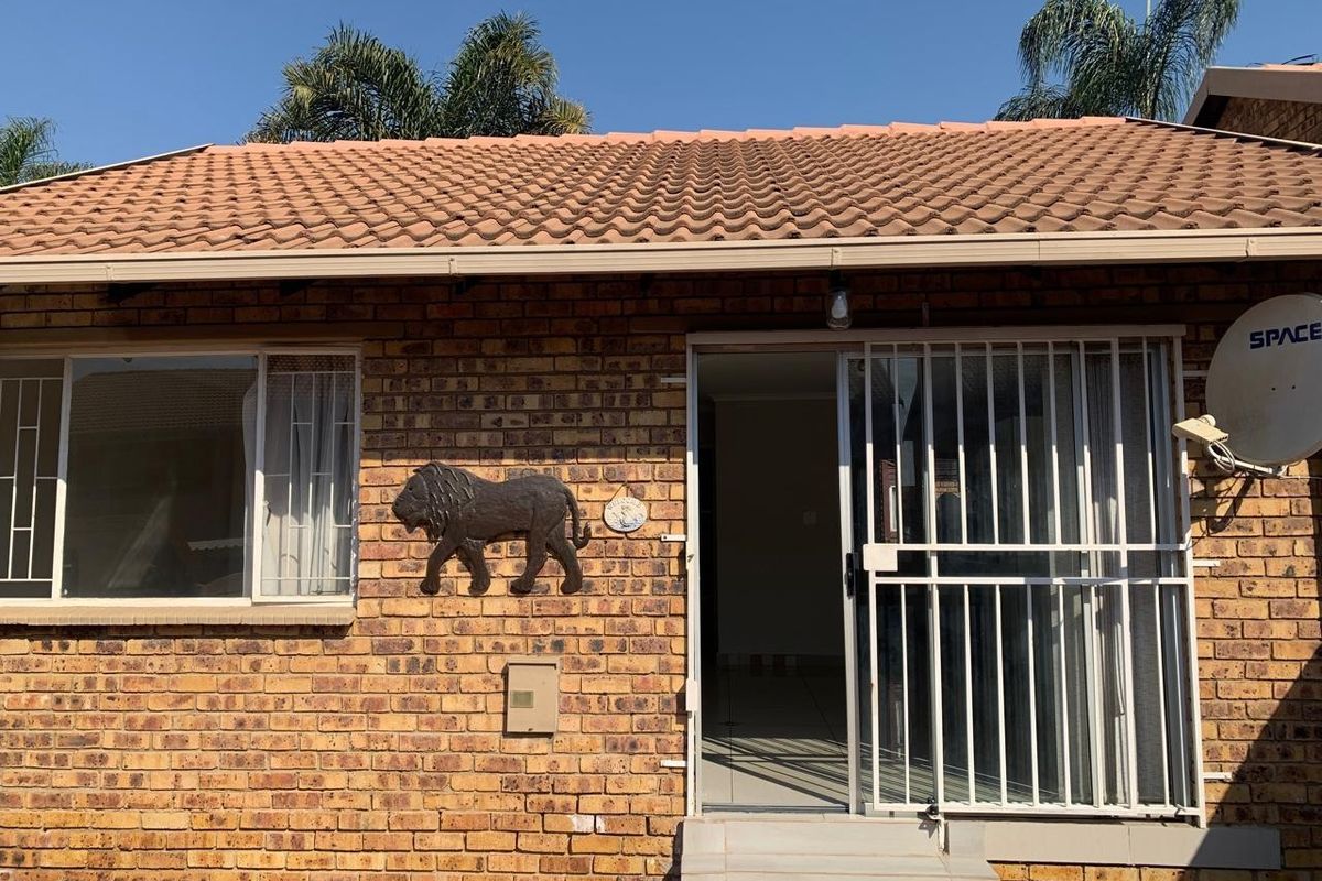 Rear exterior view of a face brick townhouse featuring a tiled roof, security gate, and sliding door access.