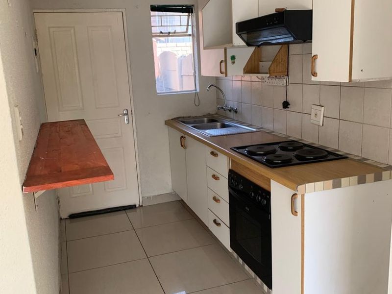 Compact kitchen featuring built-in cabinetry, electric hob, oven, extractor fan, and tiled flooring. The space includes a wall-mounted breakfast bar and requires minor cosmetic updates.