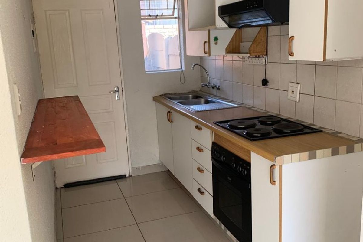 Compact kitchen featuring built-in cabinetry, electric hob, oven, extractor fan, and tiled flooring. The space includes a wall-mounted breakfast bar and requires minor cosmetic updates.