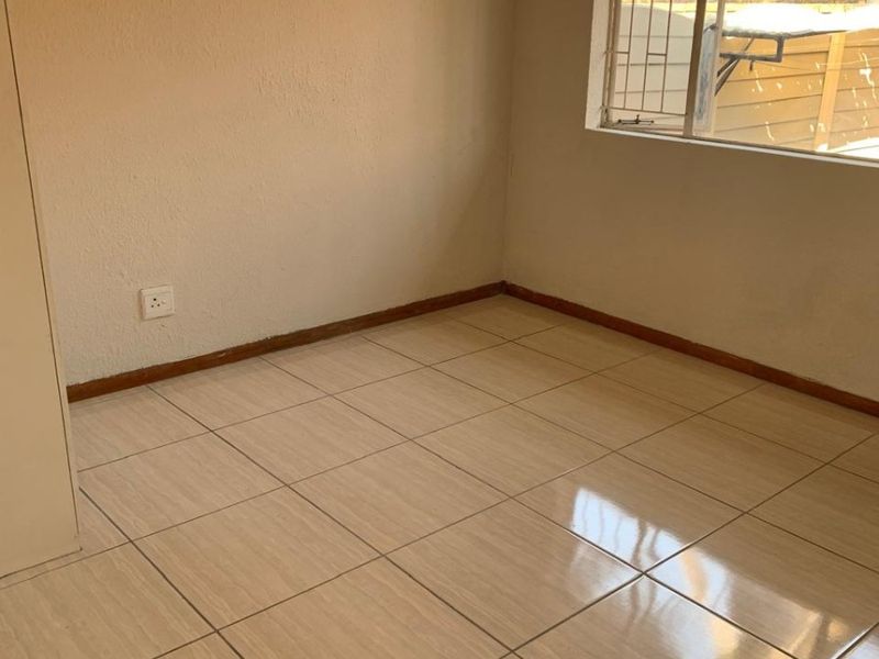 A vacant bedroom featuring neutral ceramic floor tiles, built-in cupboard storage, and a window fitted with security burglar bars.
