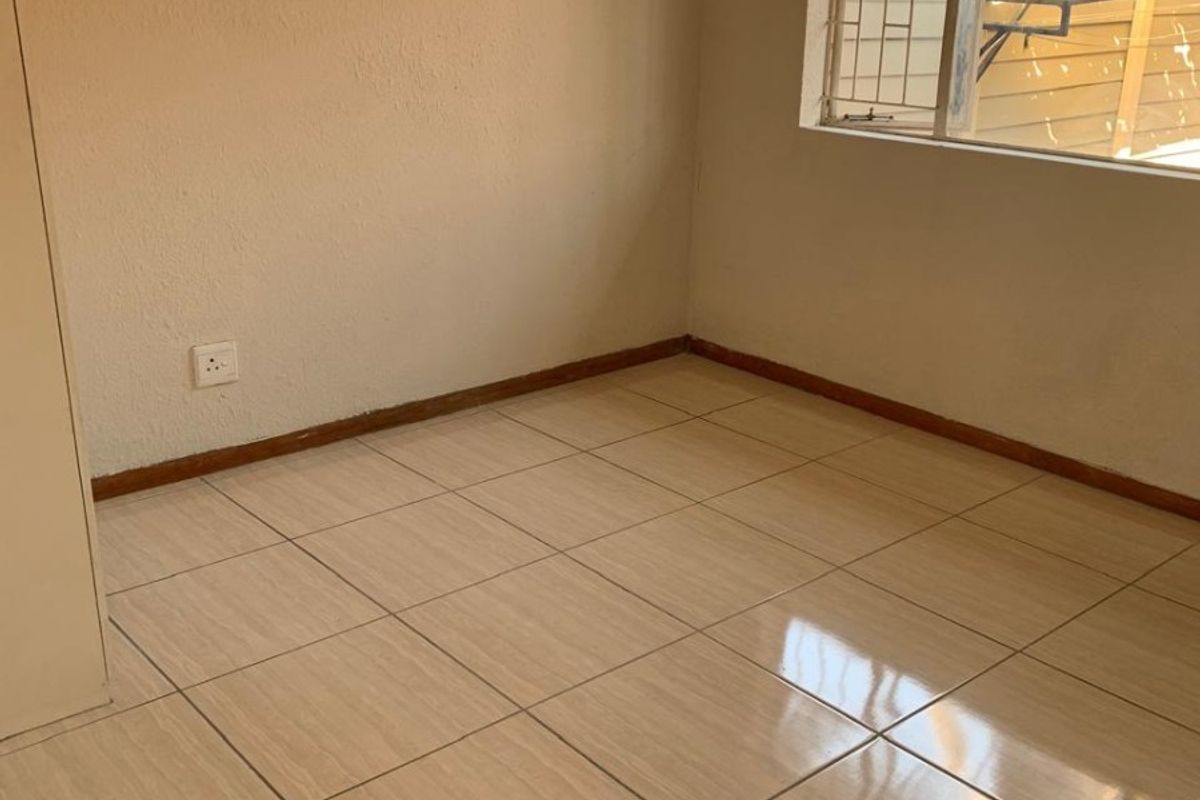 A vacant bedroom featuring neutral ceramic floor tiles, built-in cupboard storage, and a window fitted with security burglar bars.