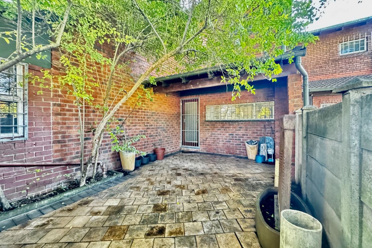 A private rear courtyard featuring brick walls, paved flooring, and a covered patio area with security gate access.